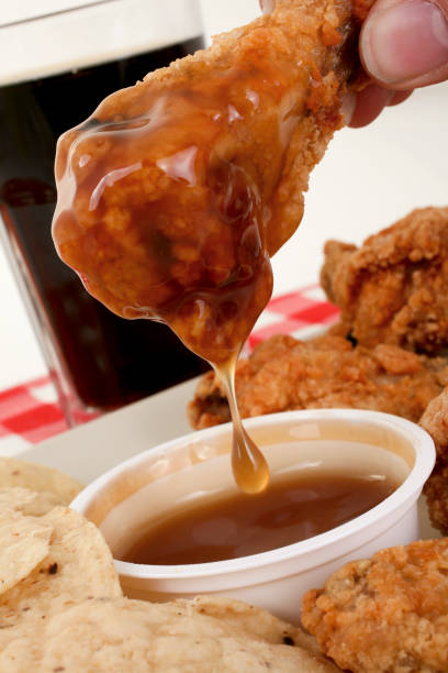 A hand holding a fried chicken wing dipped in sauce, with a side of dipping sauce and tortilla chips.