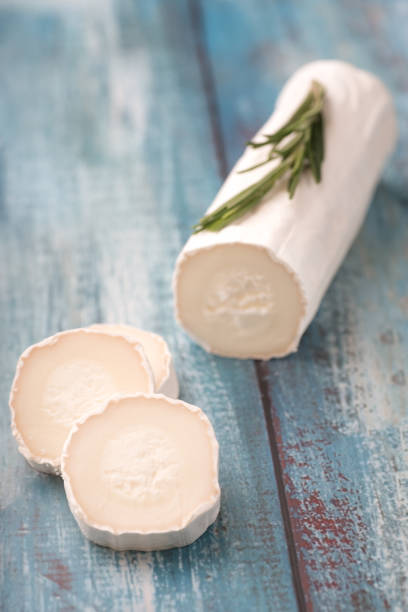 A log of soft cheese with slices cut from it, garnished with fresh herbs, on a rustic wooden surface.