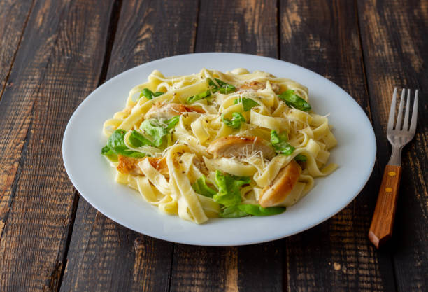 Plate of fettuccine pasta with greens and sliced chicken on a wooden table