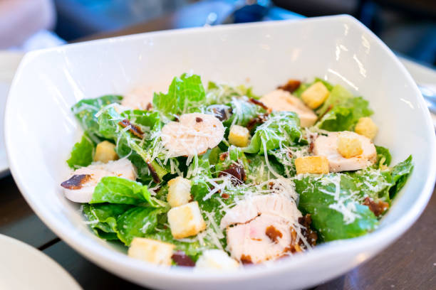 A fresh salad featuring romaine lettuce, sliced grilled chicken, croutons, and grated cheese in a white bowl.