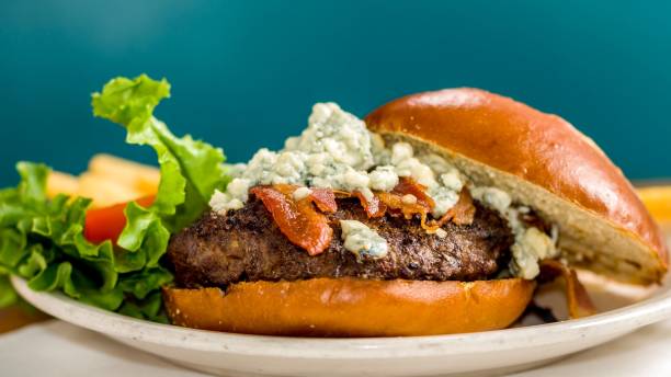 A gourmet cheeseburger topped with blue cheese and crispy bacon, served with lettuce on a plate.