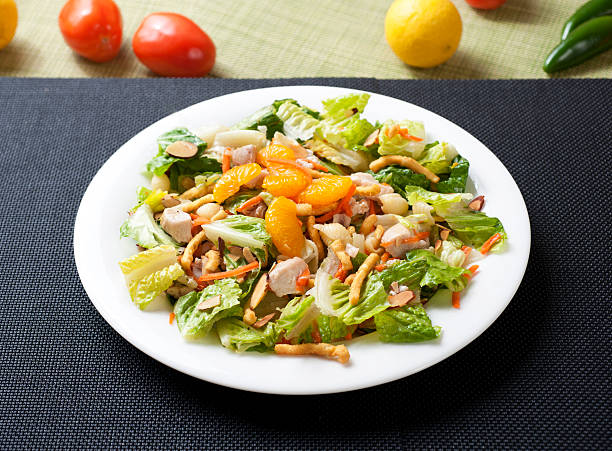 A fresh salad with Romaine lettuce, chicken pieces, mandarin orange slices, almonds, and crunchy noodles on a white plate.