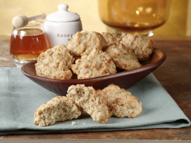 A wooden bowl filled with freshly baked biscuits beside a honey jar on a green cloth.