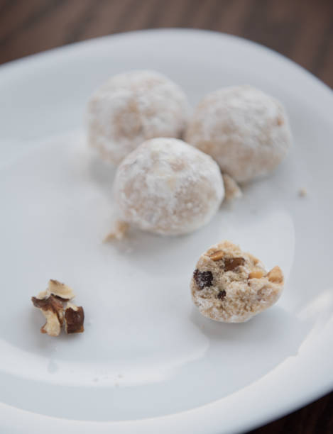 A white plate with four snowball cookies, two whole and one partially bitten, with some chopped nuts beside them.