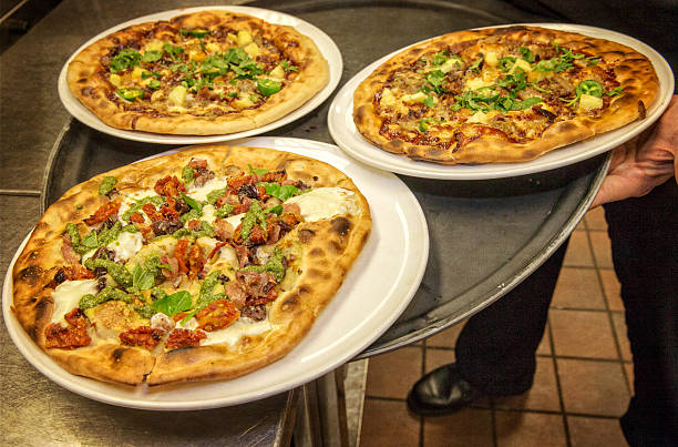 Three freshly made pizzas on large white plates held on a tray, featuring various toppings and herbs.