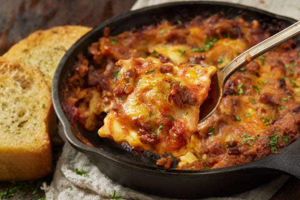 A serving of cheesy lasagna being lifted from a cast iron skillet, accompanied by slices of crusty bread.