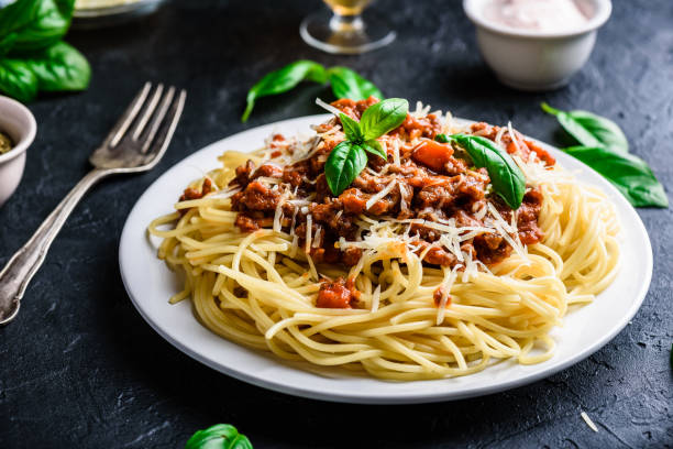 A plate of spaghetti topped with meat sauce and fresh basil leaves on a dark background