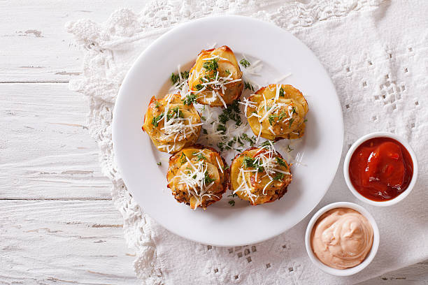 A plate of golden-brown potato cups topped with cheese and herbs, served with dipping sauces on the side.