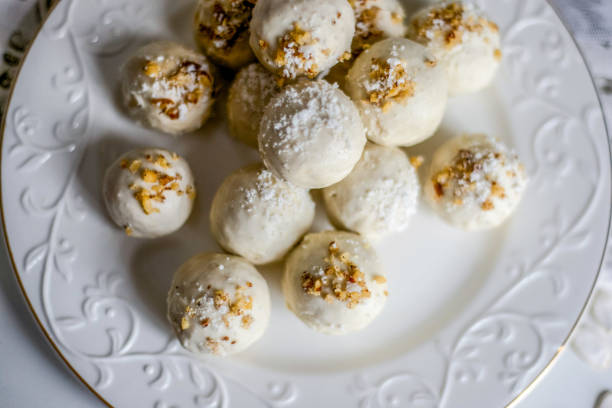 A close-up view of round white dessert balls topped with crushed nuts on a decorative white plate.