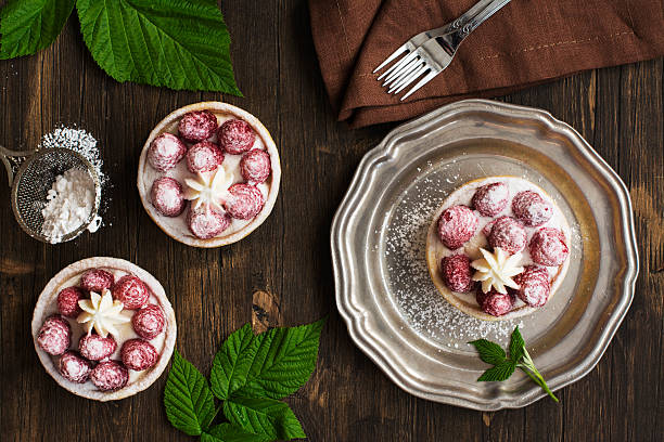 Dessert showcasing raspberry tarts on a wooden table with green leaves and a fork