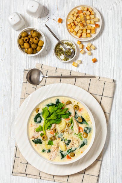 A delicious bowl of creamy chicken soup garnished with fresh herbs, surrounded by green olives and croutons.