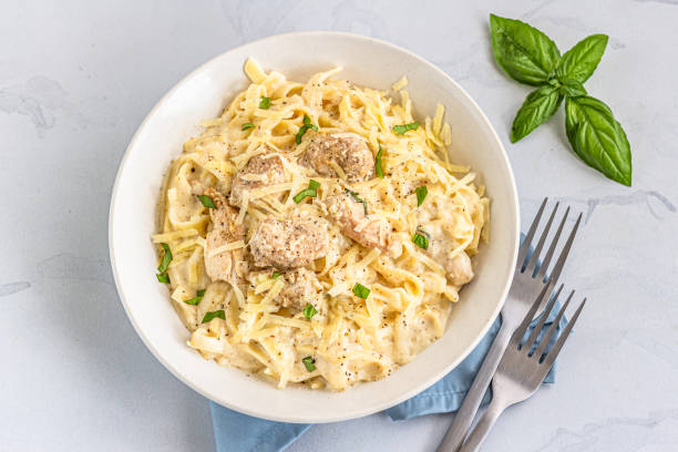 A bowl of creamy chicken fettuccine pasta topped with fresh basil and grated cheese.