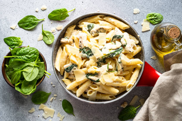 A delicious creamy pasta dish with spinach and chicken in a red pot, served alongside fresh spinach leaves and olive oil.