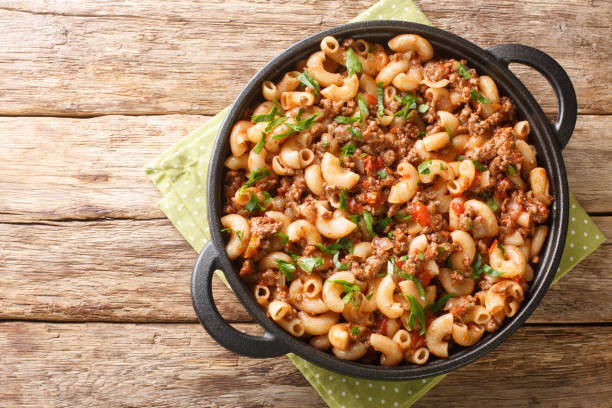 A large black bowl filled with macaroni pasta mixed with ground beef and green onions, placed on a green polka dot napkin atop a wooden surface.