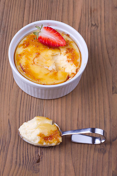 A creamy crème brûlée topped with berries and mint leaves, served with two cups of coffee on a wooden table.