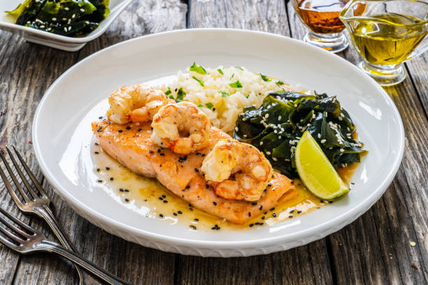 Grilled salmon fillet topped with shrimp, served with rice and seaweed on a wooden table.