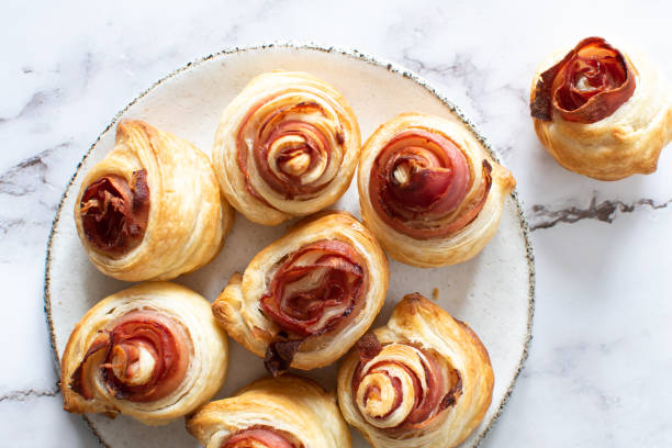 A plate of freshly baked ham and cheese spiral pastries on a marble surface.