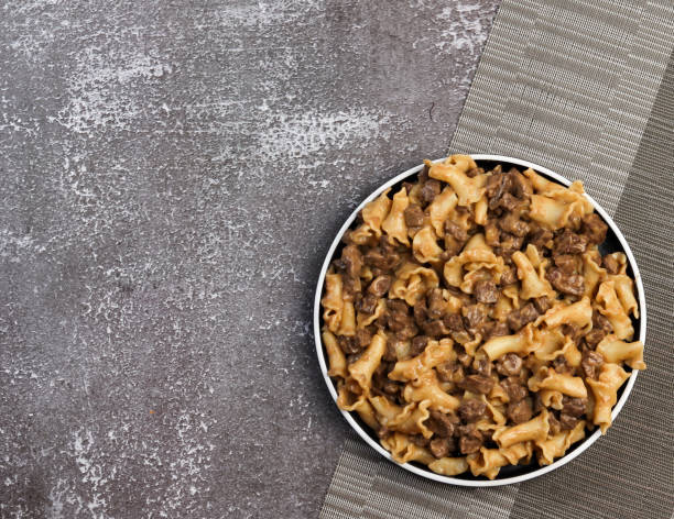 A bowl of beef and pasta dish on a textured gray surface.