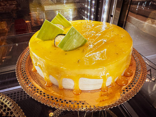 A beautifully decorated mango cake with a glossy mango glaze and triangular green decorations on top.