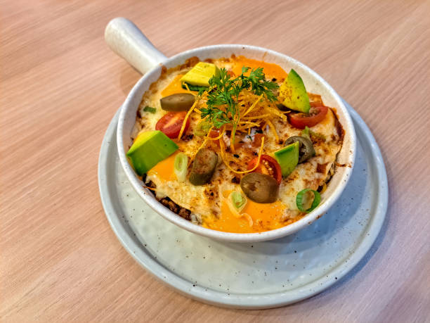 Baked dish with cheese, avocado, tomatoes, and olives in a bowl