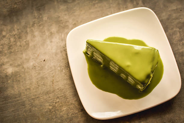 A slice of green dessert on a white plate, surrounded by green sauce.