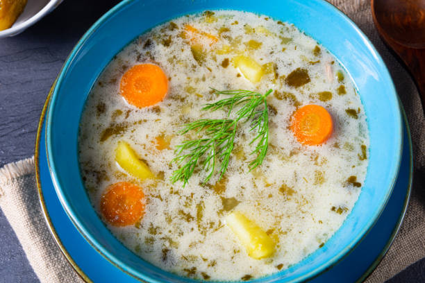 A bowl of creamy soup with carrots, potatoes, and herbs.