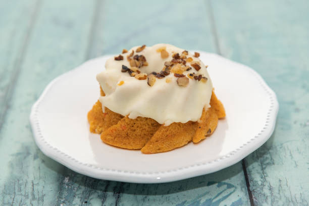 A small bundt cake topped with white frosting and chopped nuts on a white plate