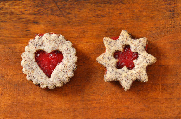 Two decorative cookies with jam filling on a wooden surface.