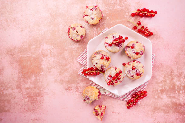 A plate of freshly baked muffins topped with red currants on a pink background.