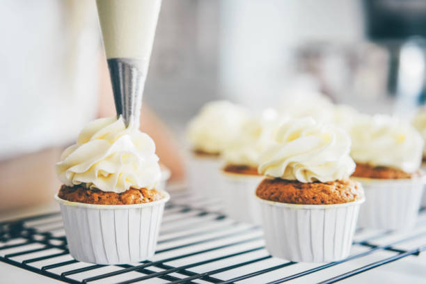 A piping bag decorating cupcakes with swirls of cream frosting.