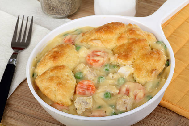 A bowl of chicken and vegetable stew topped with a golden biscuit, served on a wooden board