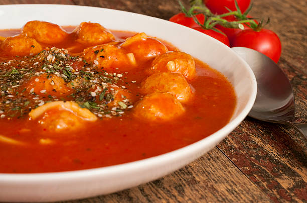 A bowl of delicious dumplings in a rich tomato sauce, garnished with herbs, alongside fresh tomatoes.