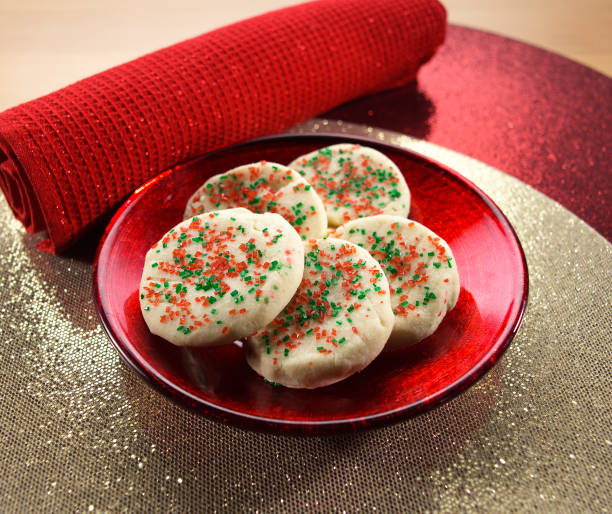 A plate of festive cookies decorated with red and green sprinkles, placed next to a red rolled napkin on a sparkling table surface.