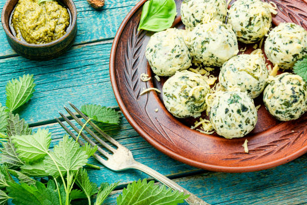 A plate of green cheese balls garnished with herbs, accompanied by a bowl of pesto on a rustic wooden table.