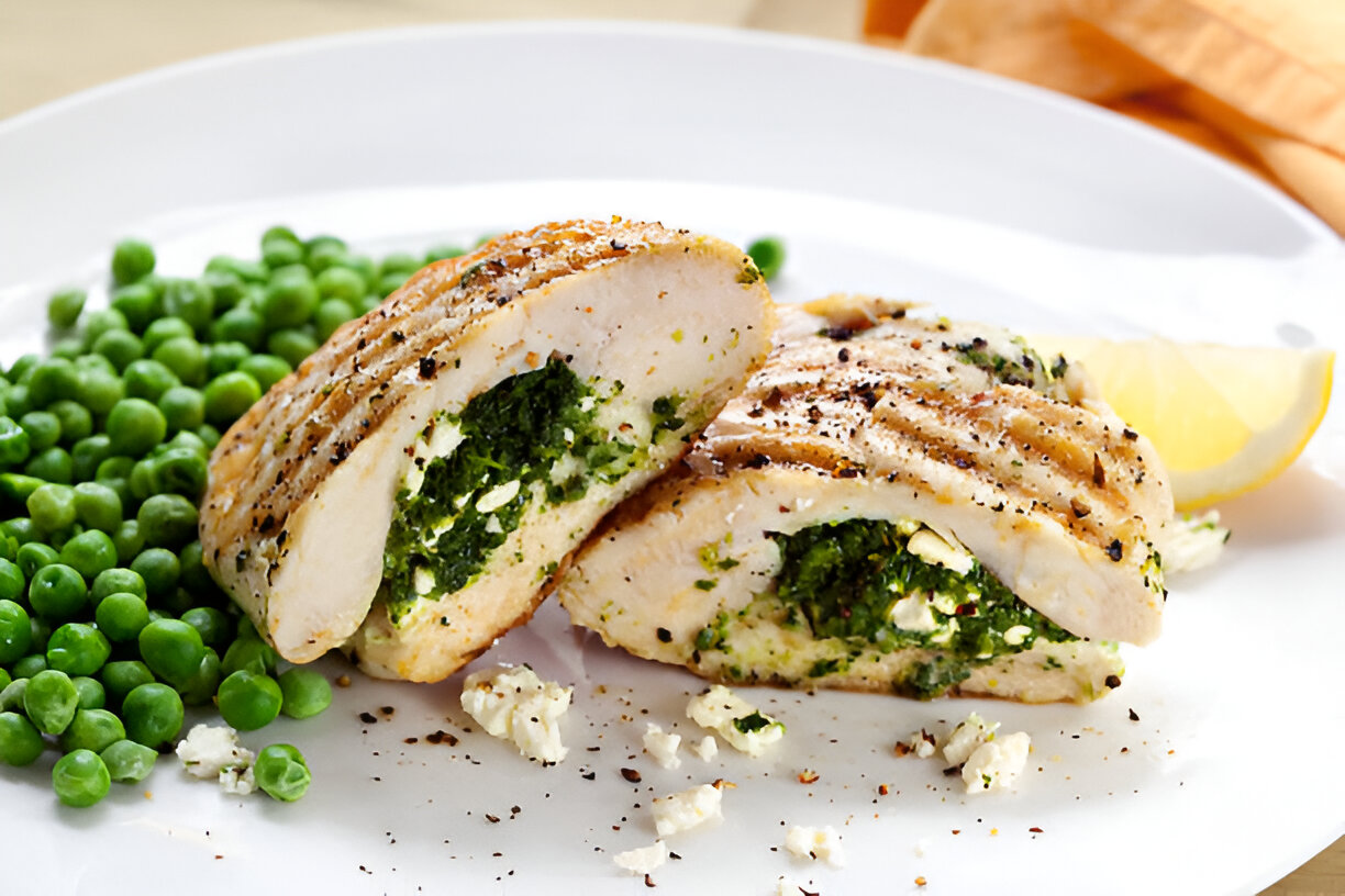 Grilled chicken breast stuffed with spinach and feta cheese, served with green peas and a lemon wedge.