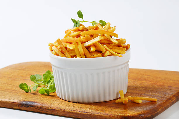 A white ramekin filled with crispy golden French fries, placed on a wooden cutting board with a sprig of fresh herbs.