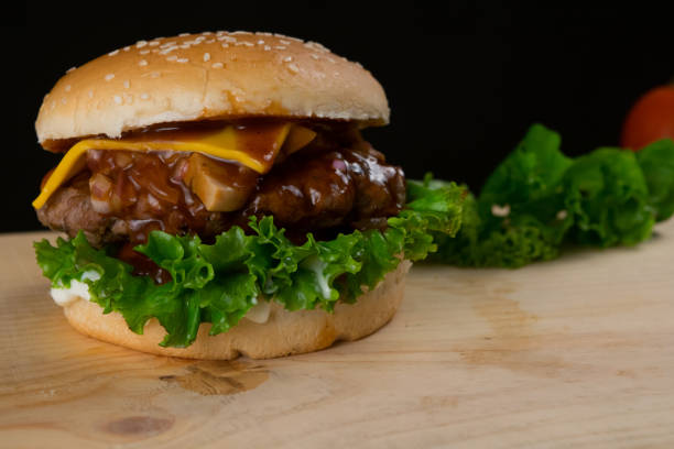 A delicious burger with sesame seed bun, cheese, lettuce, and barbecue sauce on a wooden surface.