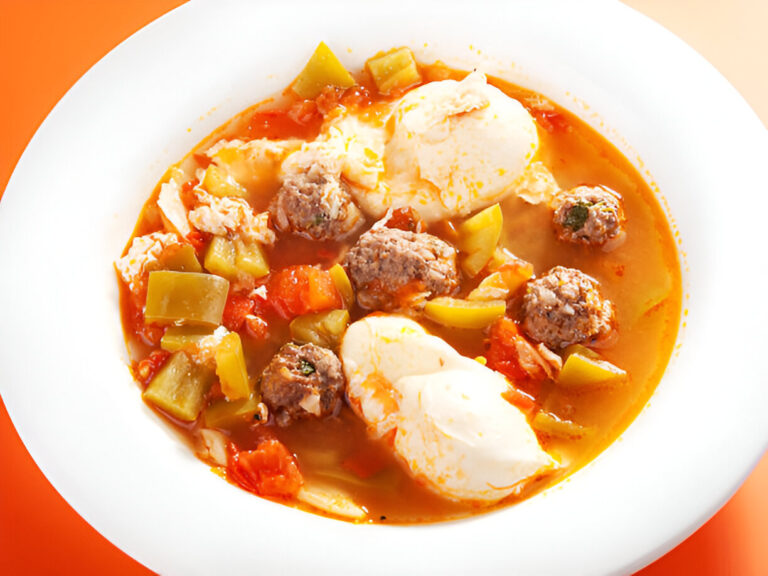 A bowl of hearty meatball soup with vegetables and poached eggs