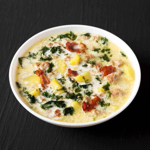 A bowl of creamy soup with kale, potatoes, and bits of bacon on a black background.