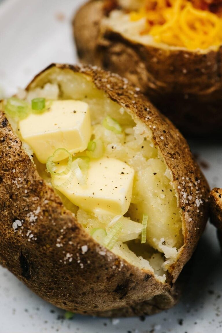 A close-up of a baked potato topped with butter and green onions, sprinkled with salt and pepper.