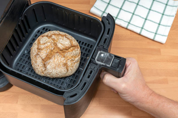 A hand holding an air fryer basket with a loaf of bread inside.