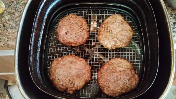 Four browned meat patties cooking in an air fryer.