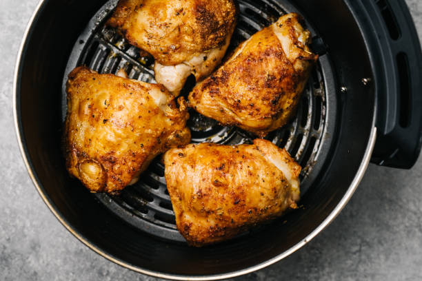 Four juicy and golden-brown chicken thighs in an air fryer basket.