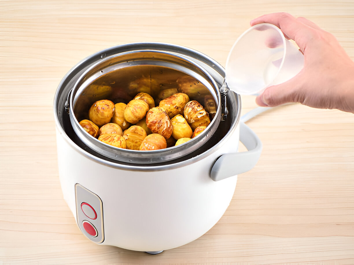 A person pouring water into a small electric steamer filled with golden baby potatoes.