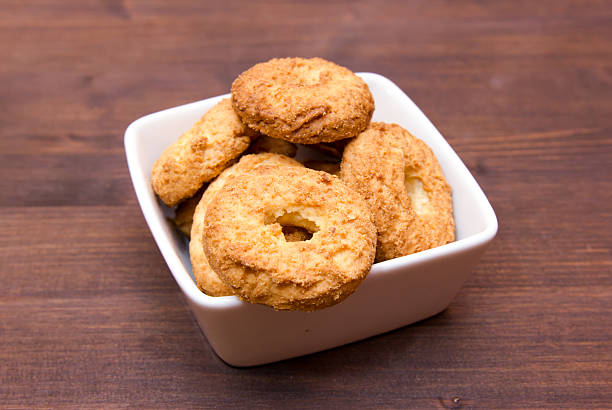 A white bowl filled with golden-brown cookies on a wooden surface.