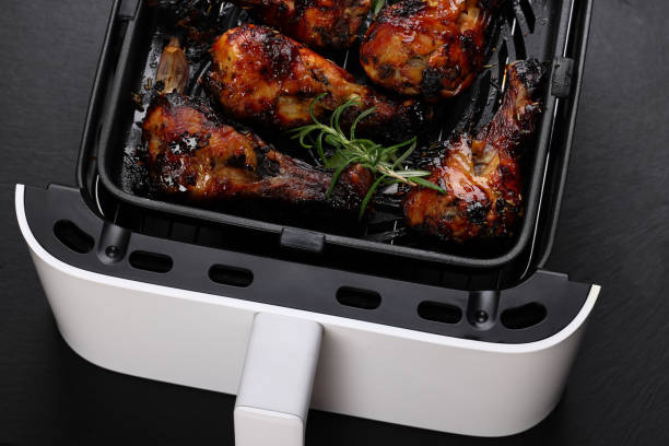 A close-up of crispy, grilled chicken drumsticks in an air fryer with a sprig of rosemary on top.