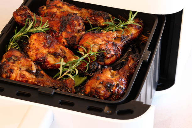 Air fryer basket with golden-brown chicken drumsticks garnished with fresh rosemary