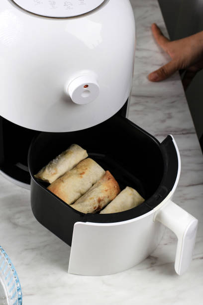 An air fryer with wrapped food inside the basket on a marble countertop.