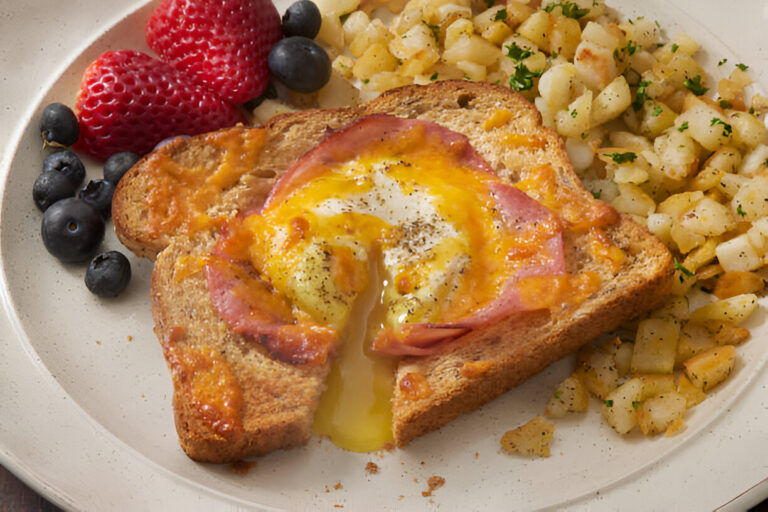 A delicious plate featuring a toasted slice of bread topped with melted cheese, ham, and a runny egg, served with blueberries, strawberries, and diced hash browns.