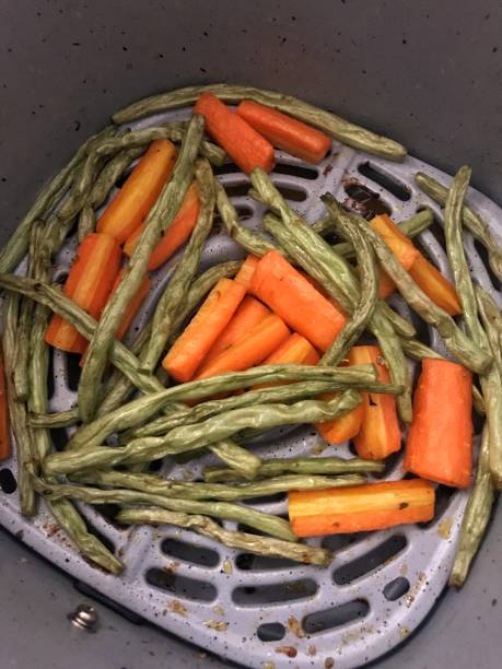 A mixture of green beans and orange carrots in an air fryer basket.